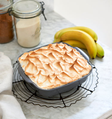 Banana pudding with a torched meringue topping, served in GreenPan ovenware with bananas in the background