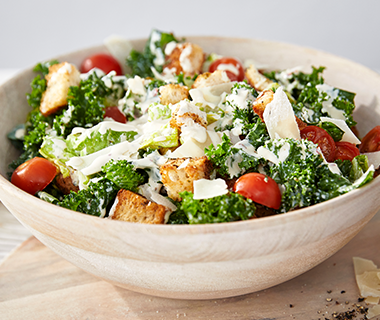 A bowl of kale Caesar salad with homemade croutons prepared using the GreenPan Premiere Titanium Cutlery 12-Piece Knife Block Set with walnut handles. 