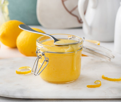 Vibrantly yellow lemon curd in a flip-top jar, curls of lemon rind in the background